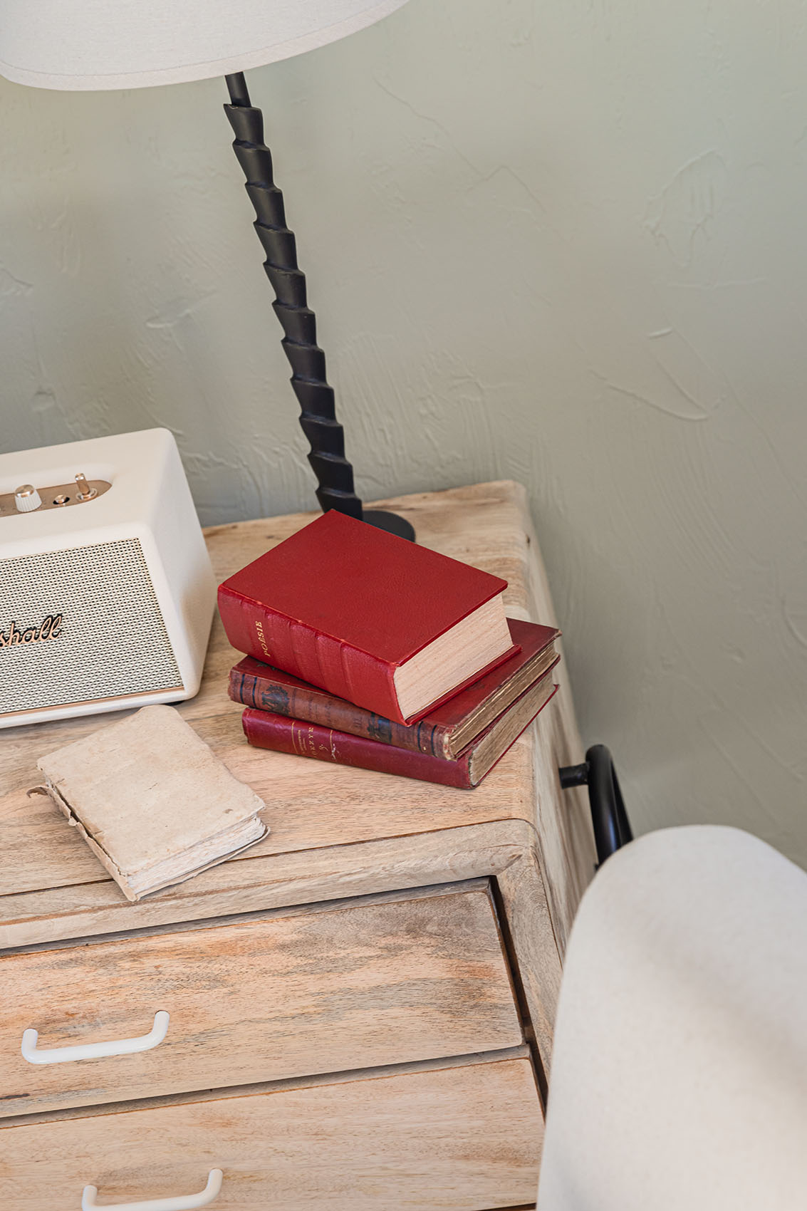 Raw wood bedside table with old red-bound books, worn notebook and Marshall speaker