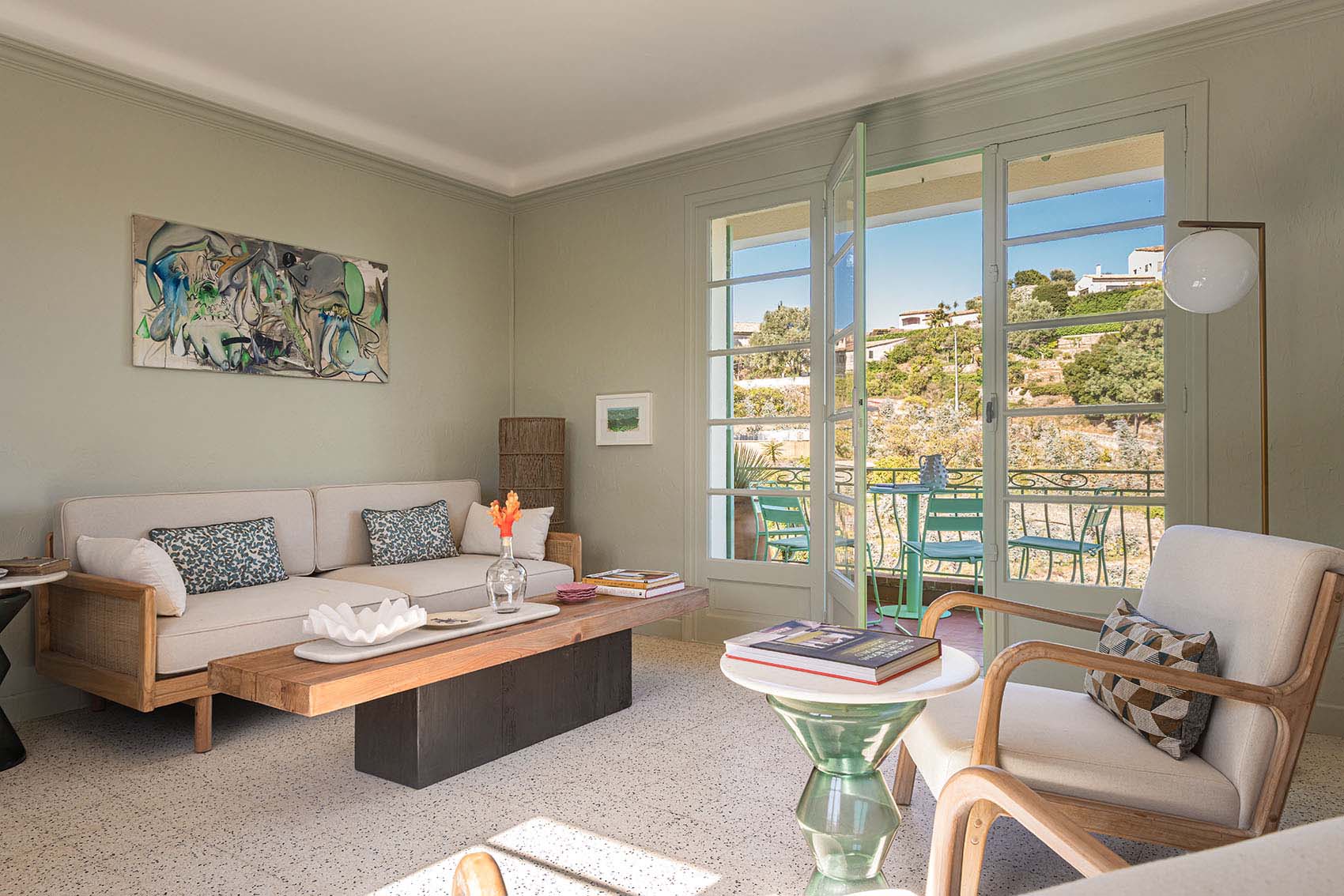 Living room with colourful abstract canvas, sofa, wooden coffee table and open French doors to balcony
