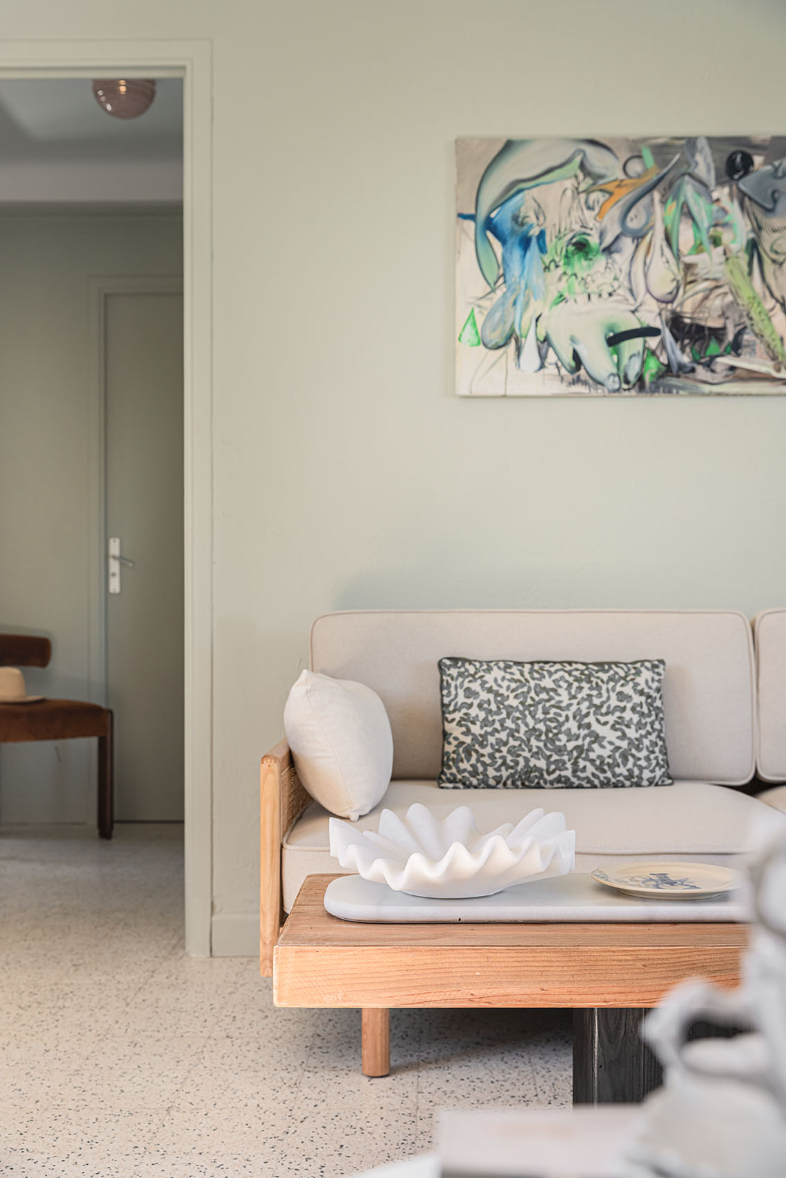 Linen sofa with leopard cushion, white sculptural giant clam on coffee table and abstract canvas beyond