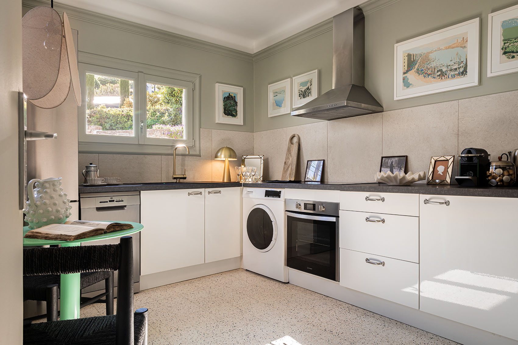 White L-shaped kitchen with terrazzo floor, Côte d'Azur watercolour prints and small round green table