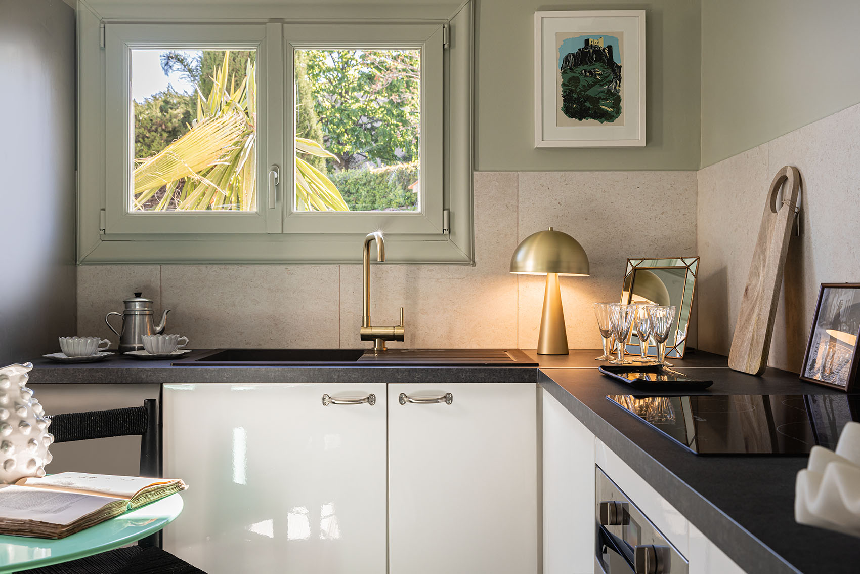 Kitchen counter with gold faucet, mushroom lamp, crystal glasses and palm-lit window above