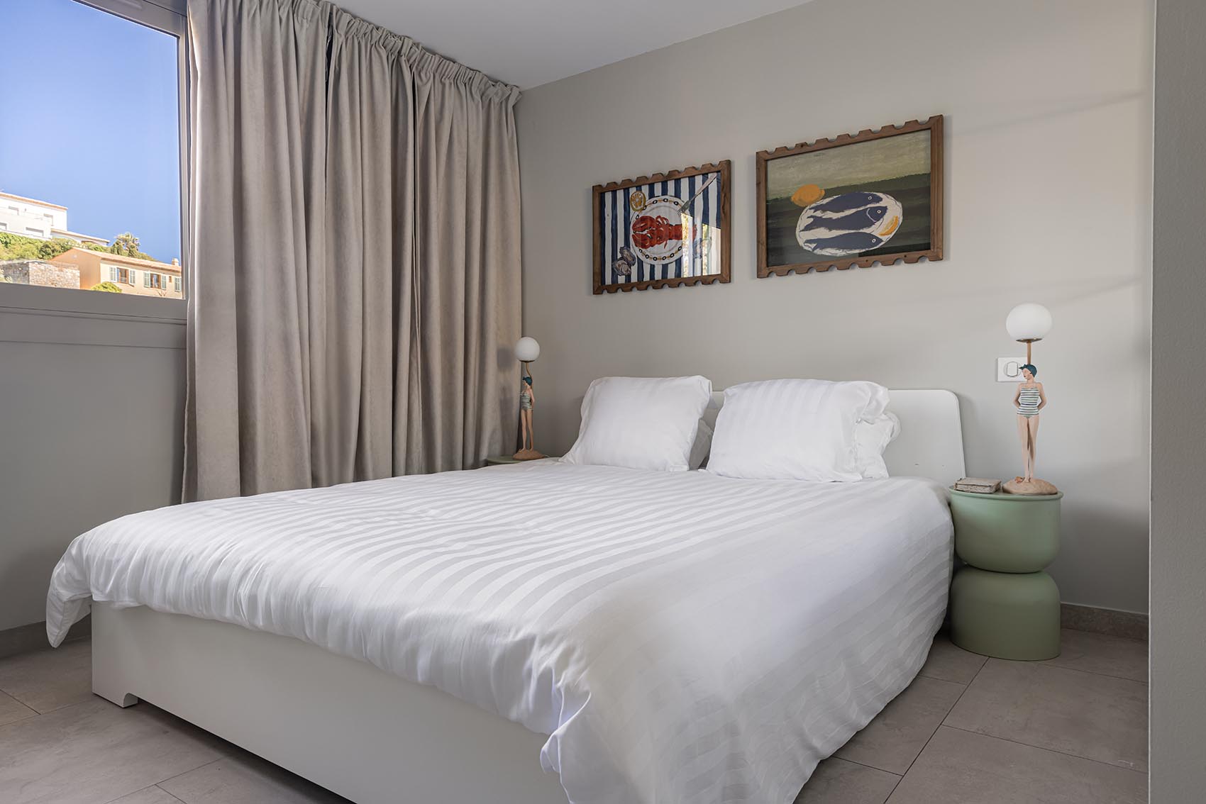 Double bedroom with white bed, two framed marine paintings and swimmer figurine lamps