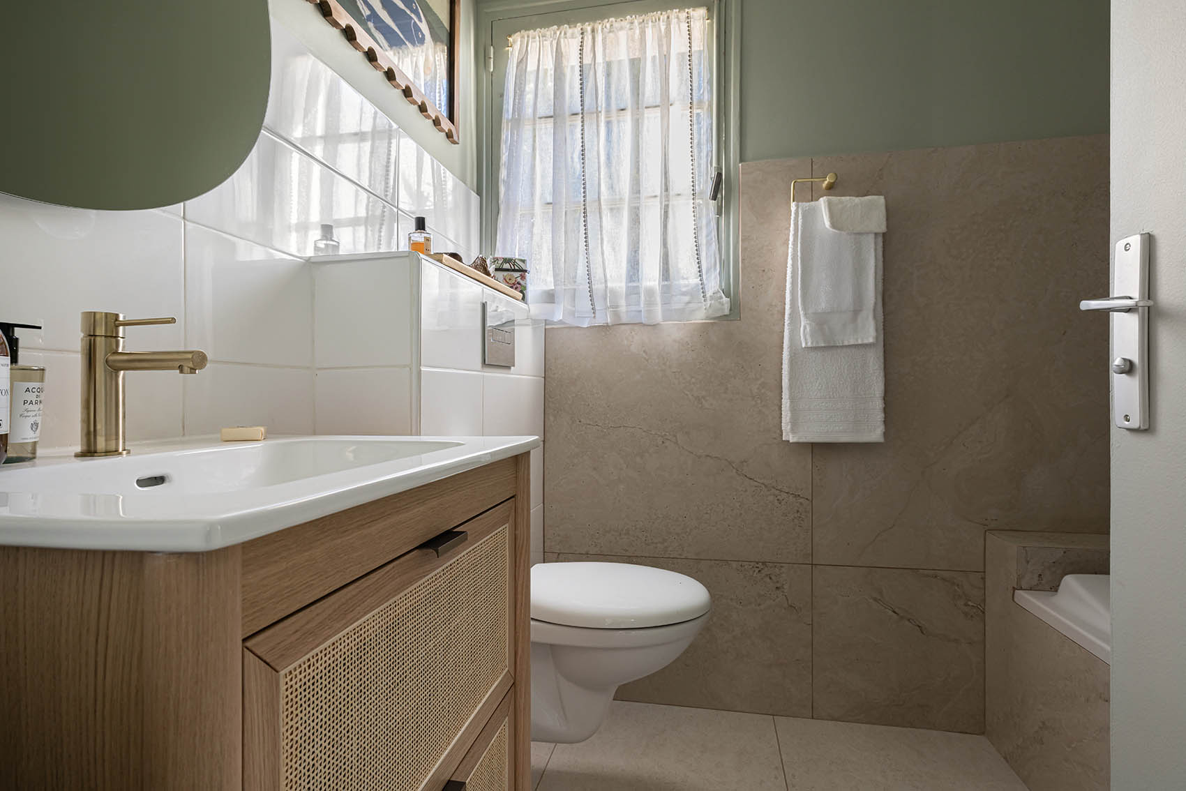 Bathroom with green walls, cane-panelled wood vanity, round green mirror and gold faucet