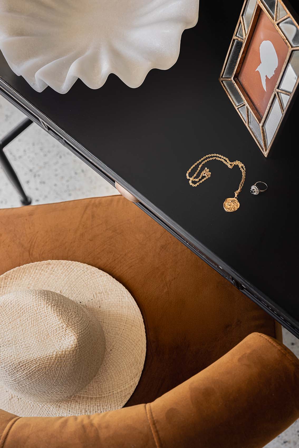 Straw hat, gold medallion necklace, ring and cameo frame on a black table