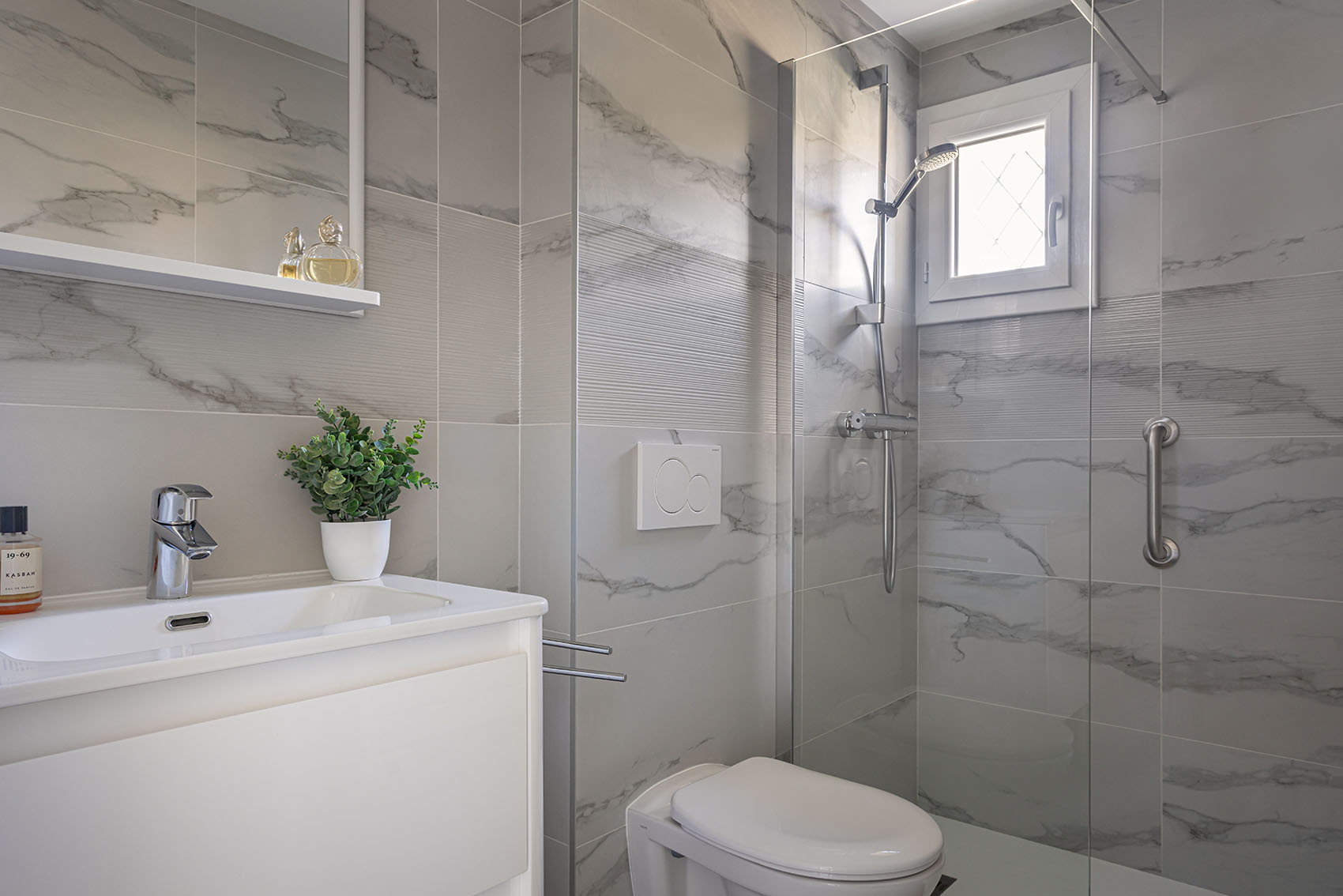Marble-effect bathroom with walk-in shower and small green plant on the shelf