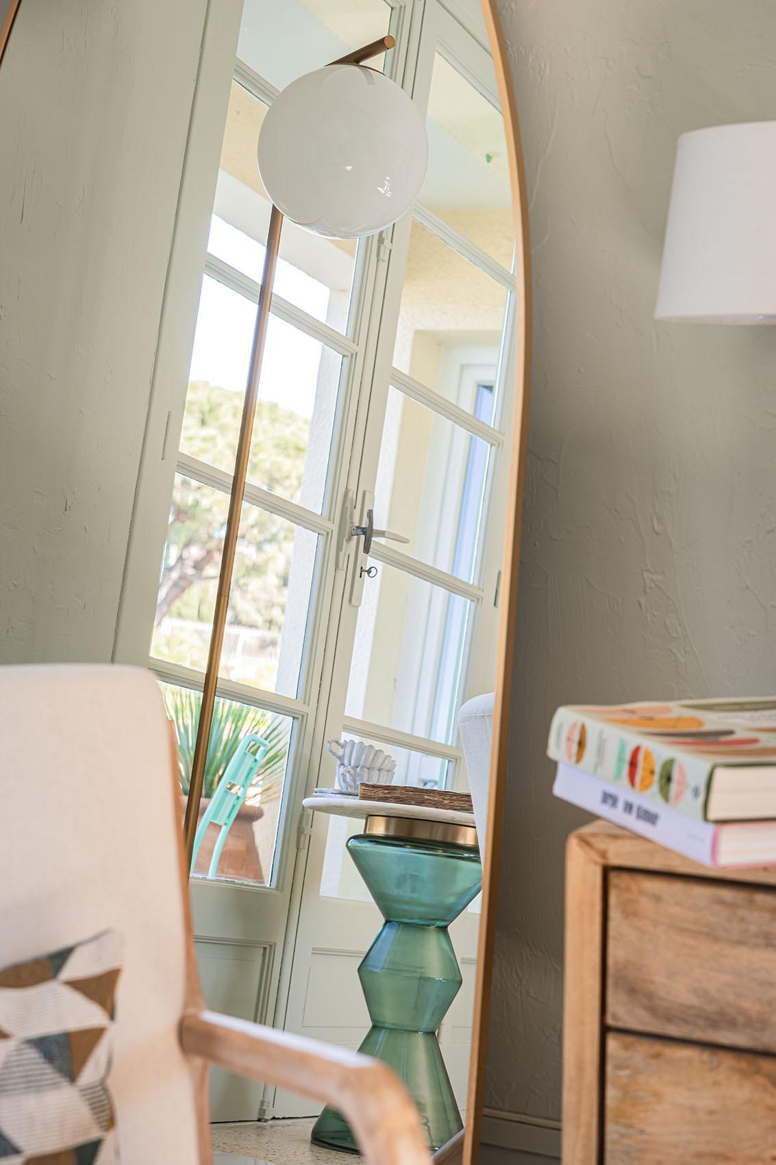 Large oval gold mirror reflecting the room, globe lamp and open French doors