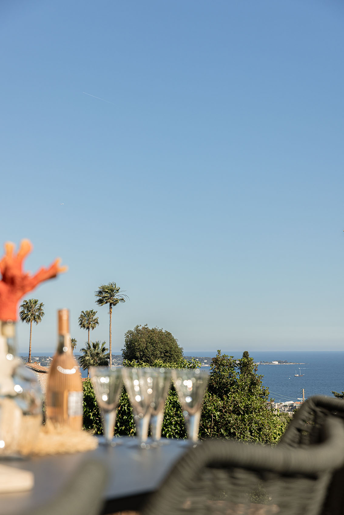 Terrace table with rosé bottle, crystal glasses and sea view between the palm trees