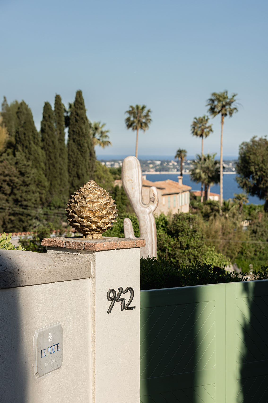 Entrance pillar with Le Poète plaque, golden pine cone, cactus sculpture and sea beyond