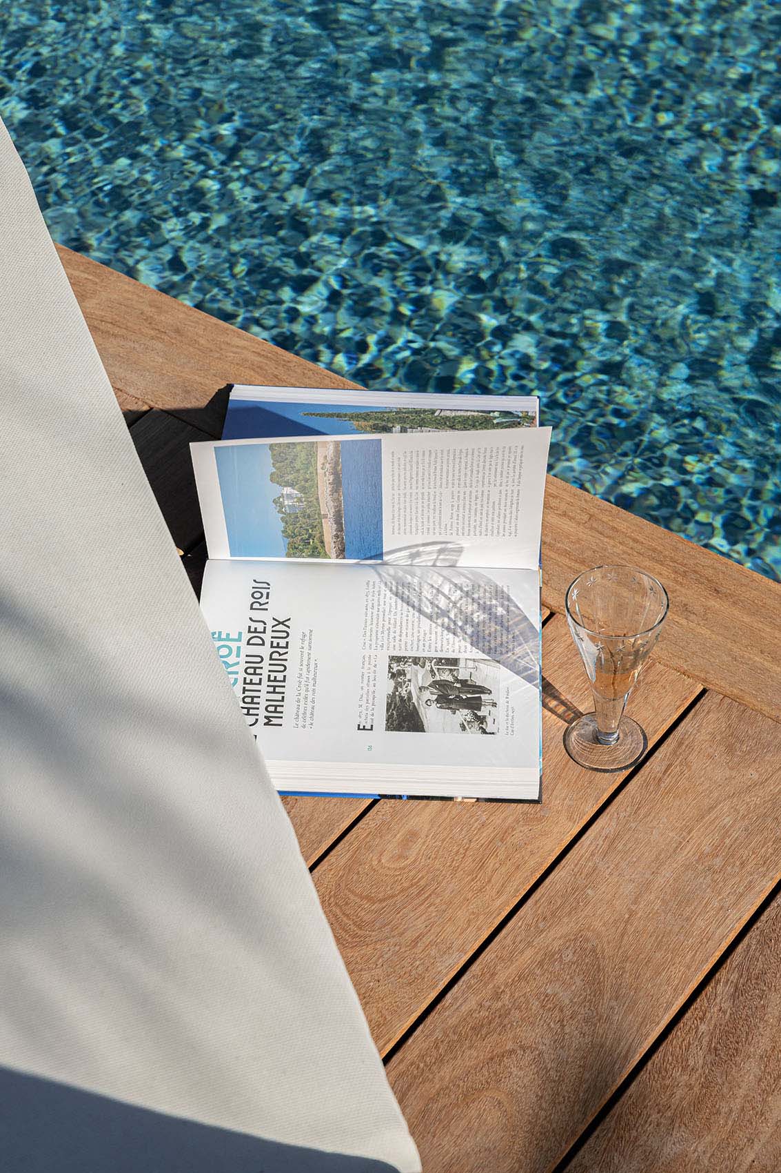 Open magazine and champagne flute on the pool deck, shimmering water beyond