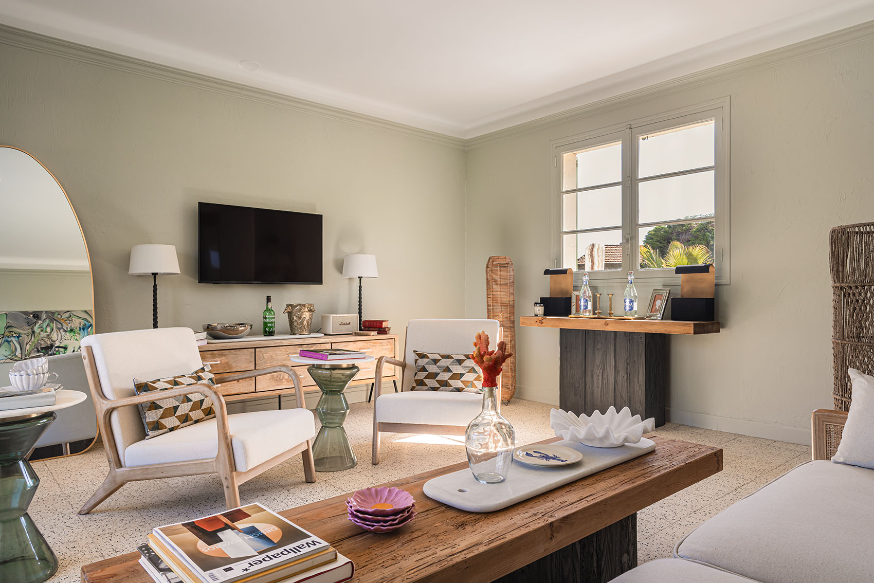 Bright living room with wooden armchairs, dark wood bar, art books and garden window